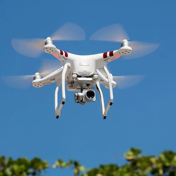 White quadcopter drone hovering against a blue sky